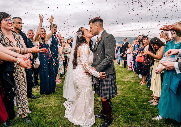 Newlyweds kiss during an outdoor confetti throw at a Scottish wedding planned by Pebblefish Occasions & Events.