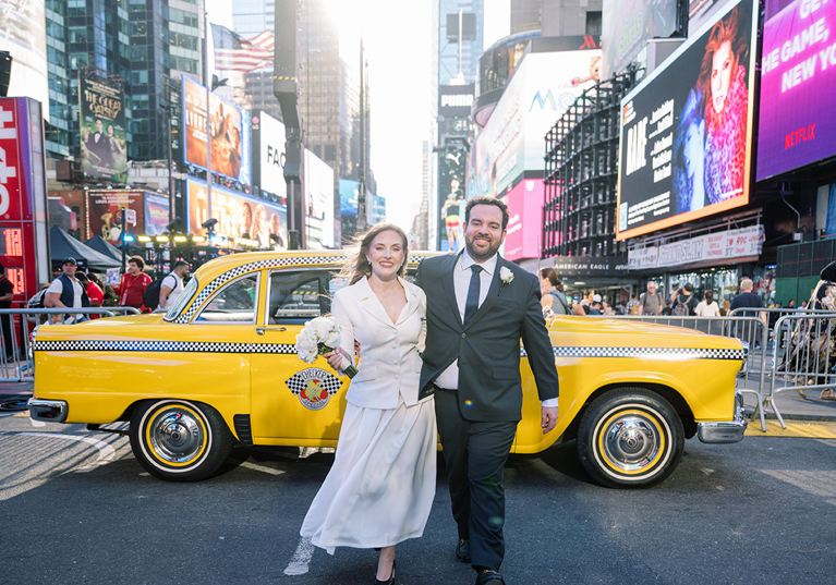 Newlyweds posing in front of a yellow taxi in Times Square, New York City wedding photos
