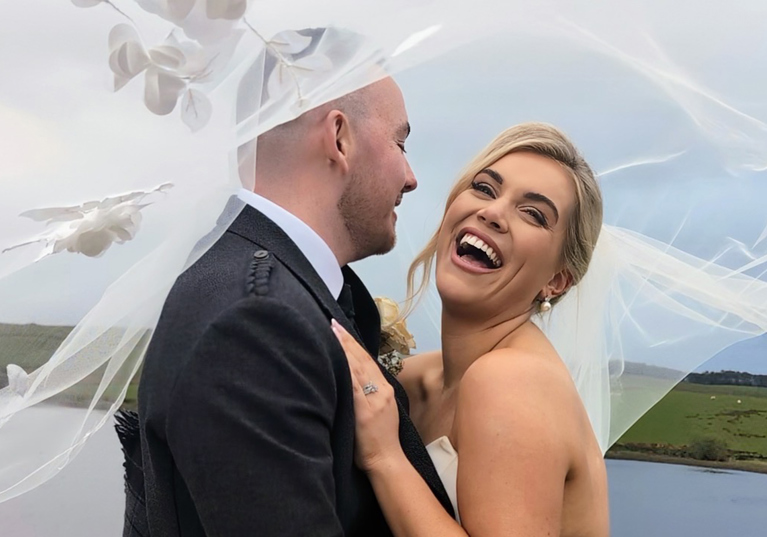 Bride laughs as her and her groom pose beneath veil by Millar Moments.