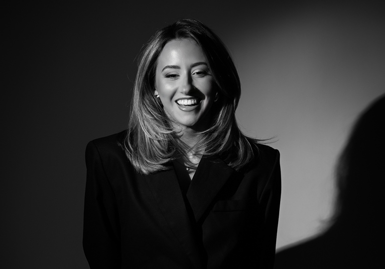 Elise, owner of Ivoura, smiles in a black and white image, wearing a black fitted suit.