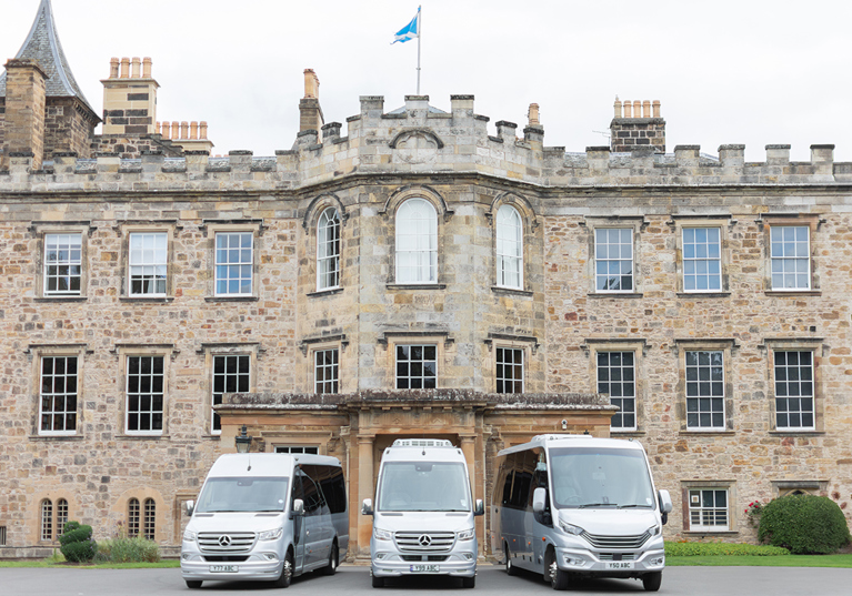 Three buses from Anderson Black Executive Travel's fleet parked outside the doors of Scottish castle wedding venue with Saltire flying overhead