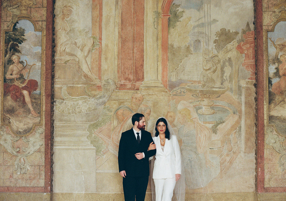 groom and bride in white suit standing in front of painted wall