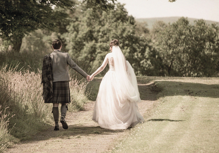Bride and groom walking hand in hand along a rural path following their wedding day, planned by DSW Weddings