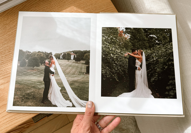 Hand holding a luxury Inkifi wedding photo album open to romantic outdoor wedding portraits of the bride and groom