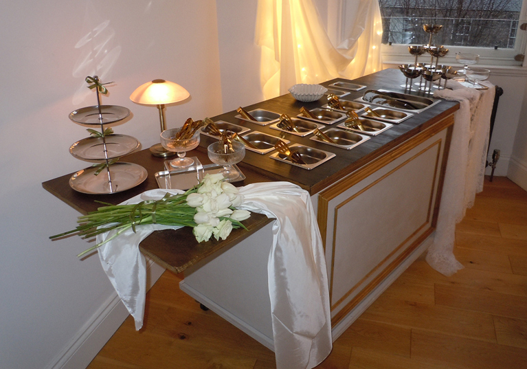 Bramble & Brie indoor wedding grazing cart with gold serving dishes, white flowers and warm ambient lighting