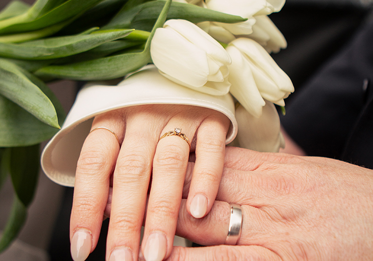Close-up of a bride and groom showing their wedding rings beside a white tulip bridal bouquet, photographed by Rscott_shoots.