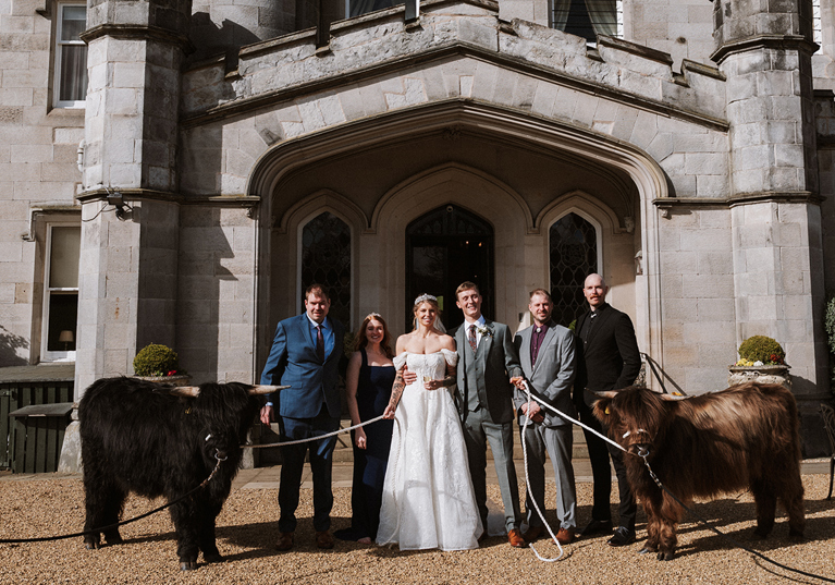 Newlyweds and members of their wedding party pose with two Highland cows from Crazy Critters Experience at Dundas Castle.