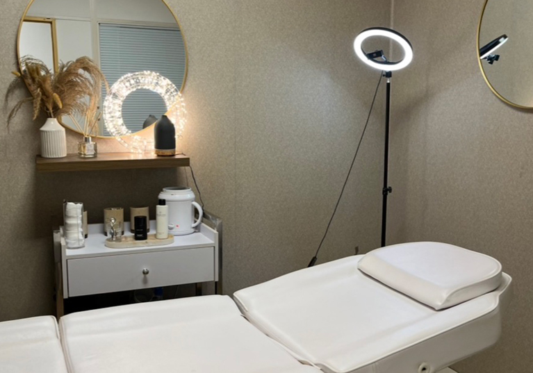 Browz & Bronze by Leah beauty treatment room with reclining bed, skincare products, mirrors and ring light.