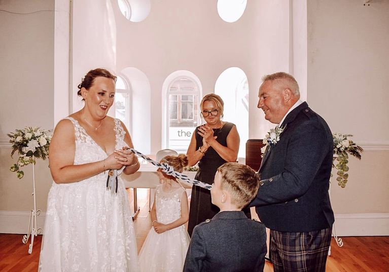 Bride and groom take part in a symbolic handfasting ceremony with their children and Fiona MacAlister Celebrant.