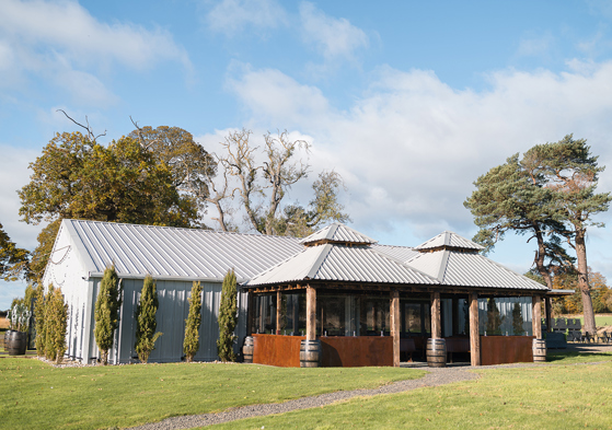 Exterior corner view of The Venue @ Duntarvie Castle in West Lothian, showing contemporary barn-style wedding venue surrounded by countryside and mature trees.