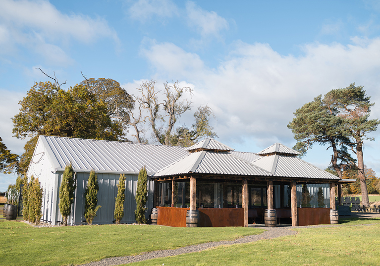 Exterior corner view of The Venue @ Duntarvie Castle in West Lothian, showing contemporary barn-style wedding venue surrounded by countryside and mature trees.