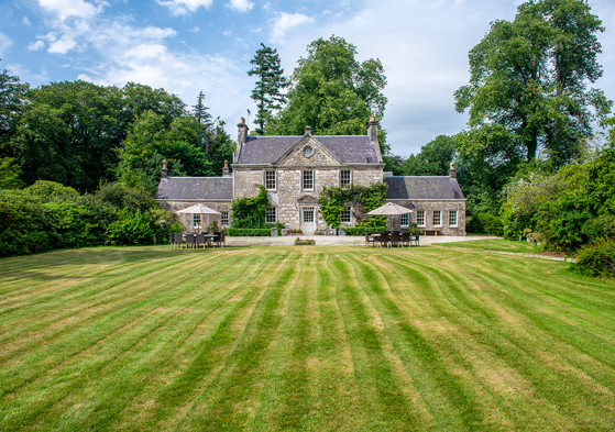 Exterior of Broomholm Manor surrounded by lawns, mature trees and private grounds in the Scottish Borders.