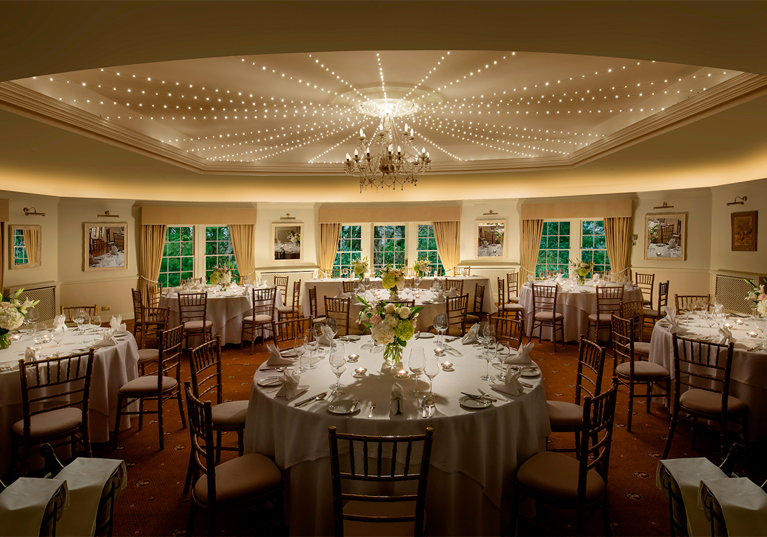 Thackray House wedding reception room set with round tables, floral centrepieces, Chiavari chairs and ceiling lights.