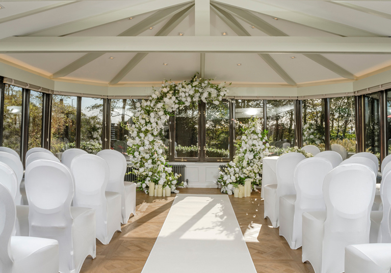 Piersland House wedding ceremony setup with white chairs, aisle runner and large white floral arch