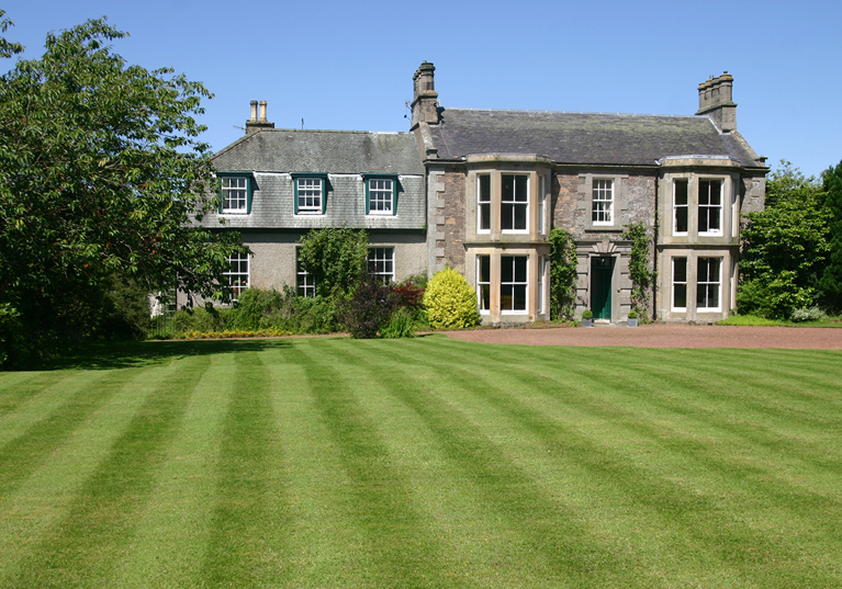 Cormiston Farmhouse exterior with manicured lawn and mature trees on a bright summer day