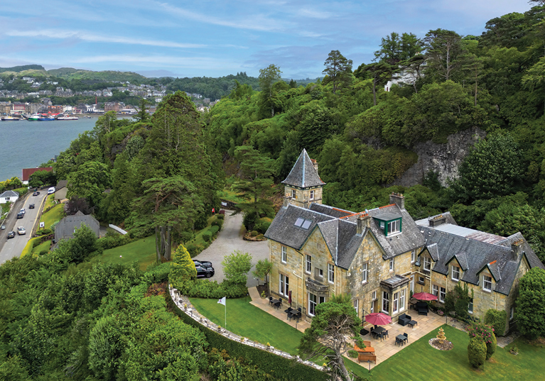 External view of Dungallan Country House in Argyll and Bute, with views of the sea and hills in background and trees behind venue.