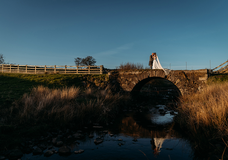 Bride and groom pose on stone bridge at Ayrshire wedding venue, Harelaw Farm