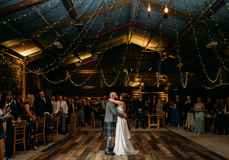 Bride and groom's first dance at Harelaw Farm in Ayrshire, beneath draped fairy lights and guests watching on in background.