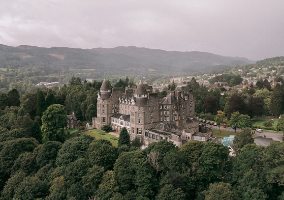 View of Atholl Palace Hotel from above with a drone, displaying its surrounding woodlands and hills in background of Pitlochry.