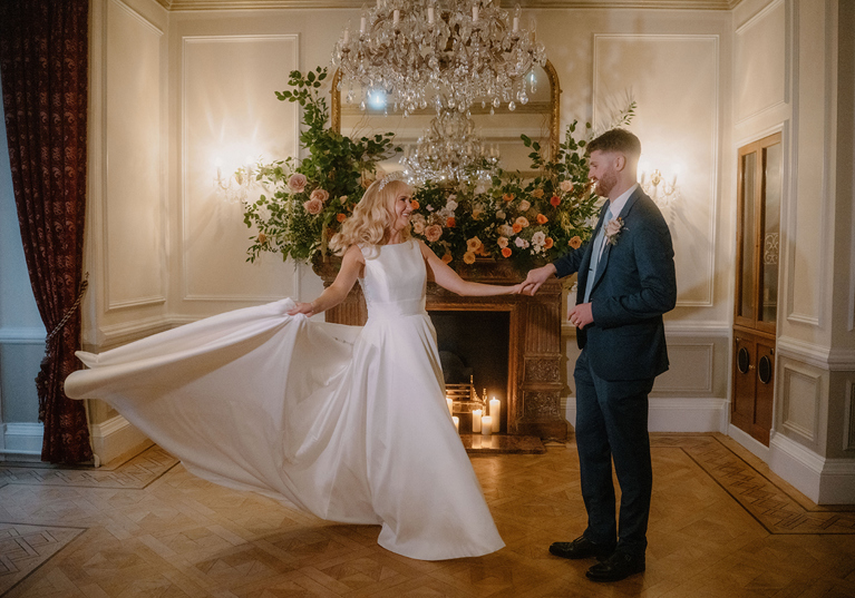 Bride and groom dancing by the fireplace in an elegant chandelier room at Auchen Castle.