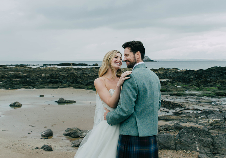 Newlyweds posing on the beach near Marine North Berwick with rocky shoreline and sea backdrop