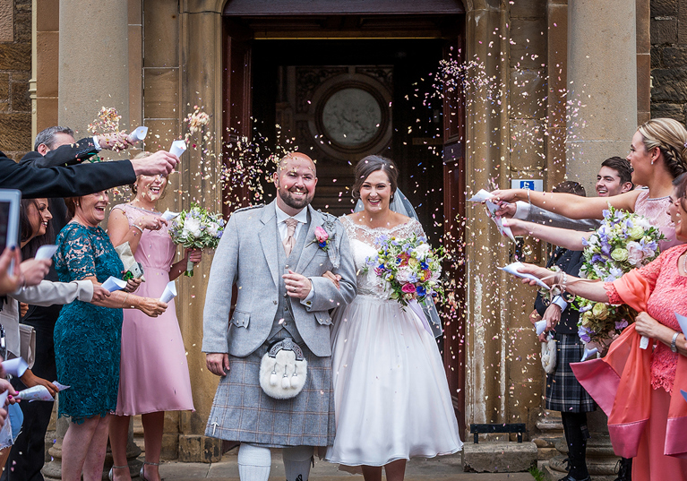 Bride and groom walking through confetti outside Newbattle Abbey College wedding entrance in Scotland