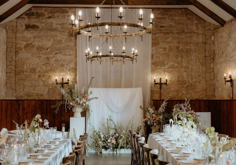 Long banquet tables with floral styling inside rustic stone reception space at Rosebery House