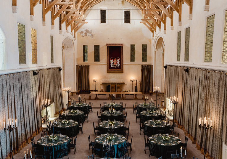 Overhead view of Stirling Castle Great Hall set for a luxury wedding dinner with dark green table linens, round tables and elegant candlelight.