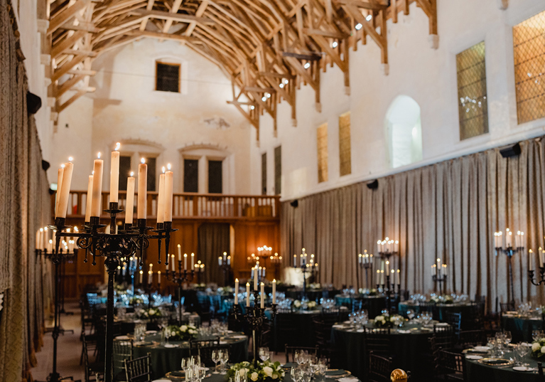 Wedding reception at Stirling Castle Great Hall featuring long candelabras, round banquet tables and dramatic medieval architecture.