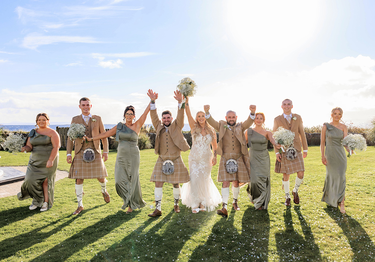 Wedding party walk together across grass on sunny wedding day at The Waterside Hotel