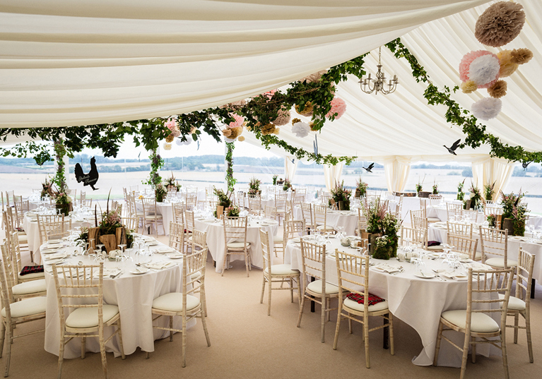 Wedding marquee reception with round tables, white linen and floral styling overlooking the East Lothian countryside at Fenton Tower