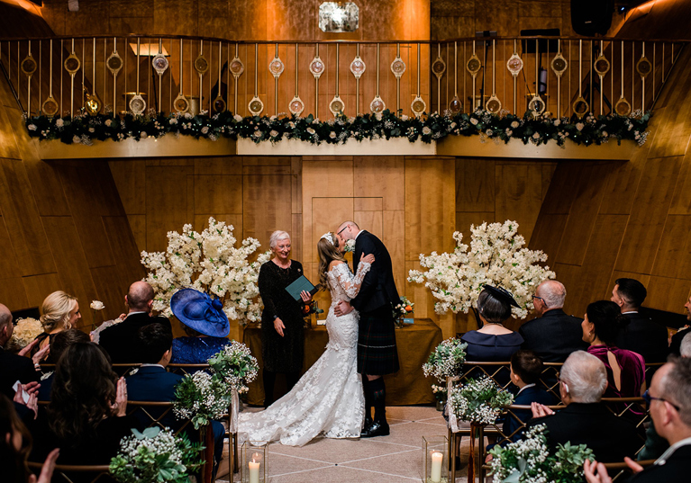 Bride and groom kiss at altar in the Ballroom on board Fingal Hotel in Edinburgh while guests clap.