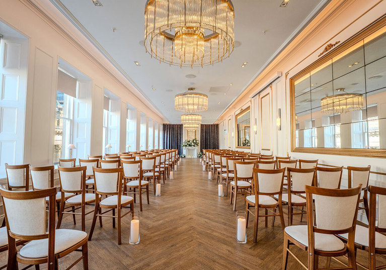 The Exchange wedding venue in Glasgow's ceremony room, with chandeliers, mirrors on walls and floral display at altar.