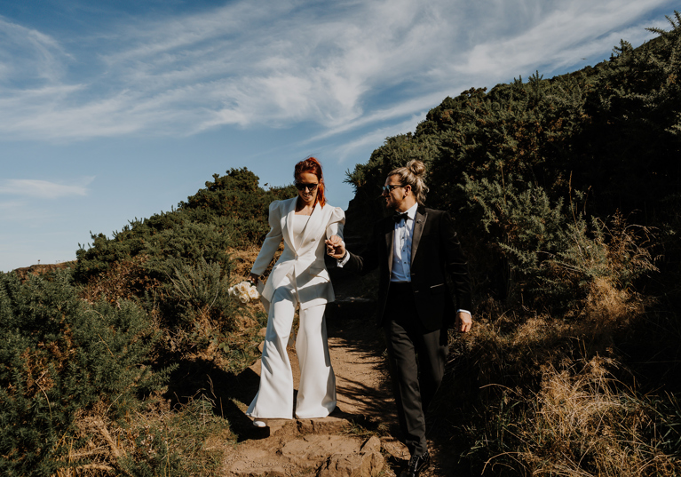 Newlyweds walking down sandy hill towards waterfront at The Scott Hotel in Edinburgh.