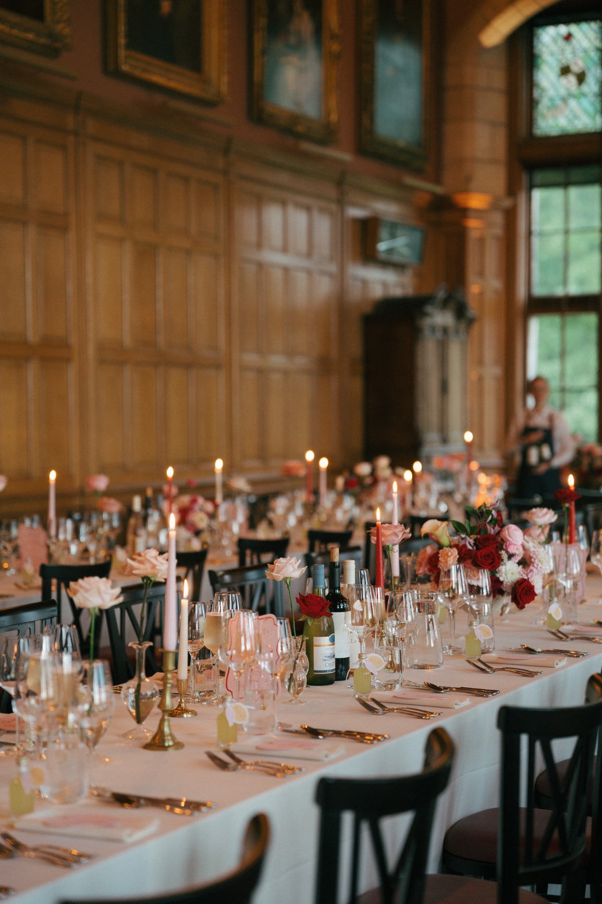 Long wedding reception tables at Barnbougle Castle decorated with red and pink floral arrangements, taper candles and elegant place settings.