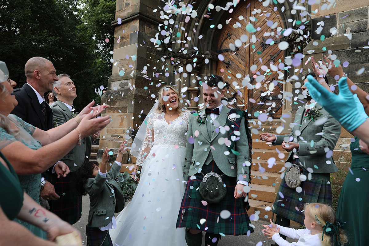 A bride and groom being showered in confetti by their guests as they leave a church