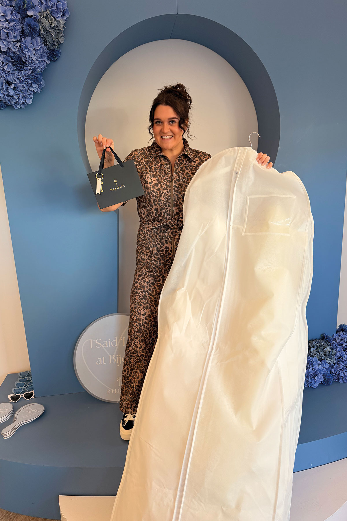 Bride collecting wedding dress at Bijoux Bridal boutique holding garment bag and bridal accessories
