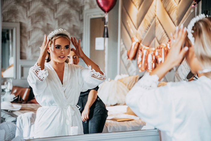 Bride wears robe and fixes headpiece in the mirror