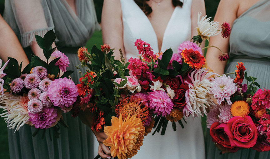 a group of women wearing wedding attire holding vibrant pink and orange wedding bouquets made by Braw Blooms