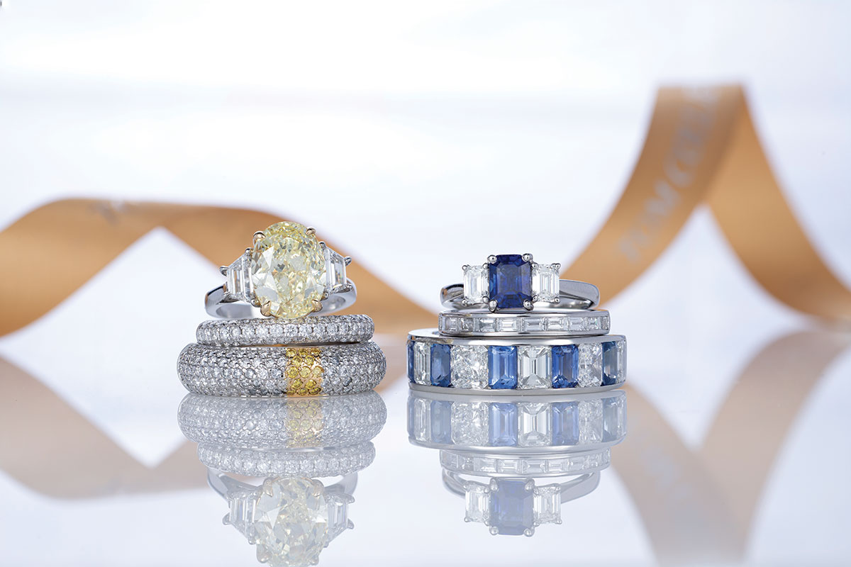 yellow diamond and sapphire rings placed on top of a mirror with gold ribbon in the background