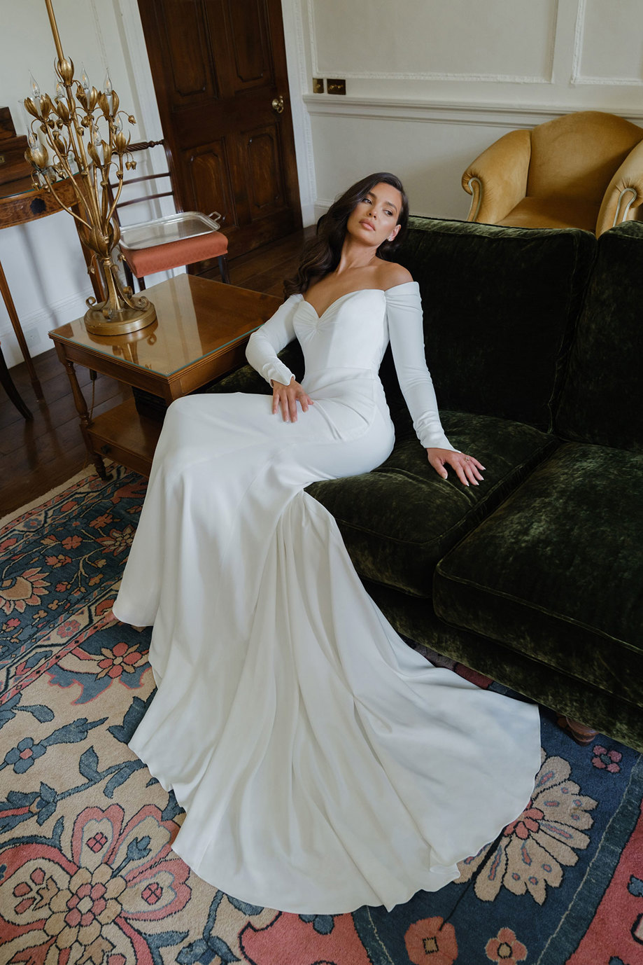 a woman wearing a wedding dress with sweetheart neckline and long sleeves by Suzanne Neville lounging on a velvet sofa