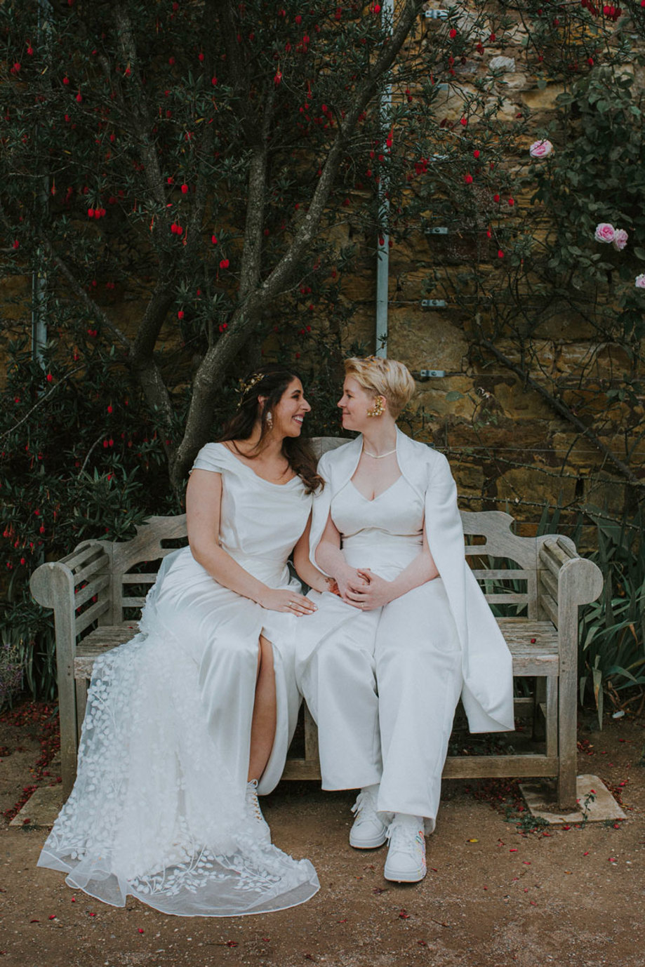 two brides smile at one another seated on a blue bench in cambo estate's walled garden