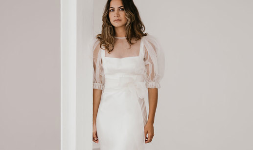 brunette woman wears a form-fitting silky whiten gown with organza puff sleeved top as an added layer