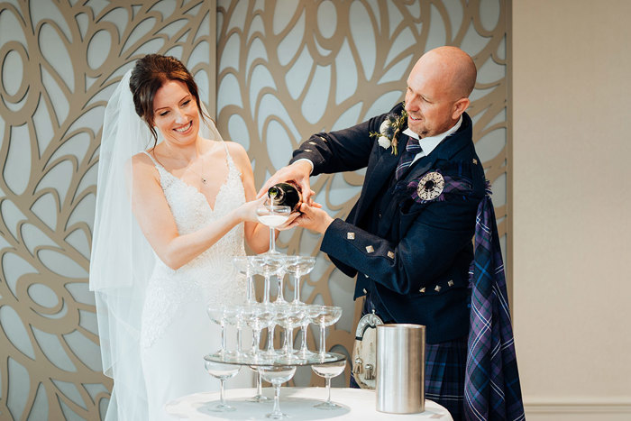 a bride and groom pour fizz into a tower of champagne coupes at Seamill Hydro 