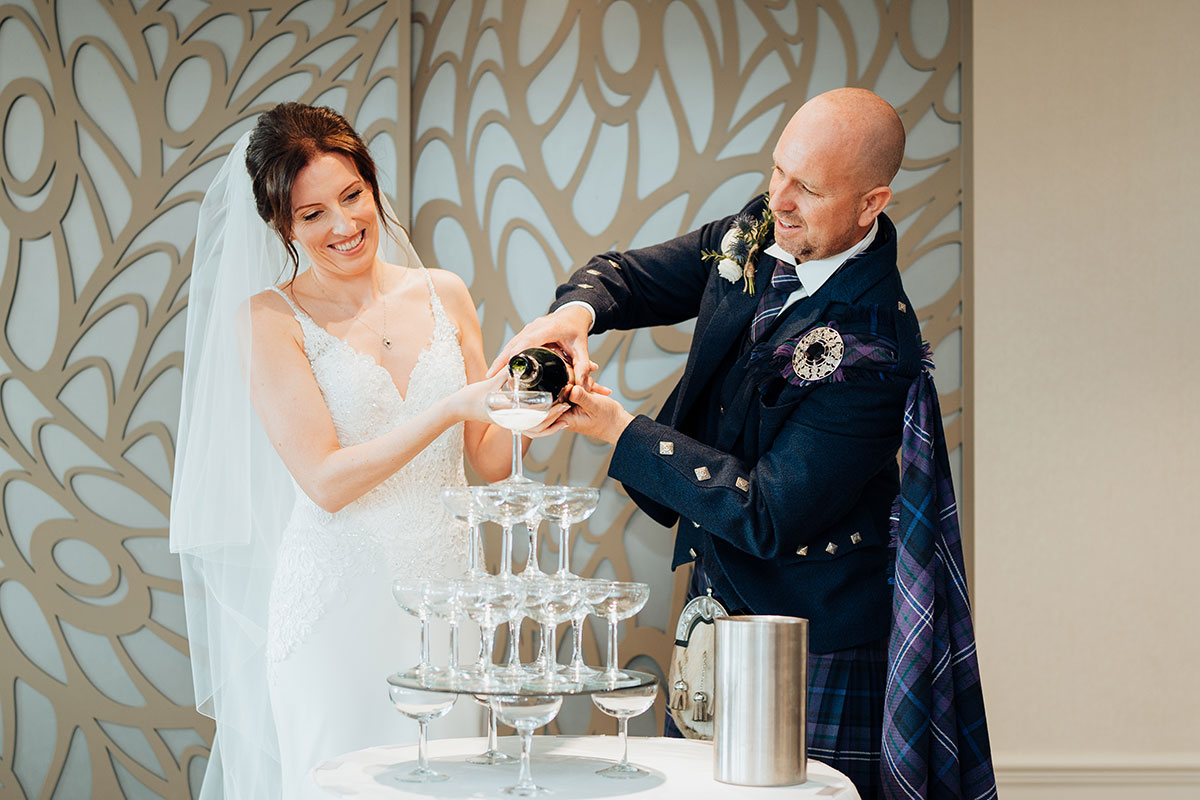 a bride and groom pour fizz into a tower of champagne coupes at Seamill Hydro