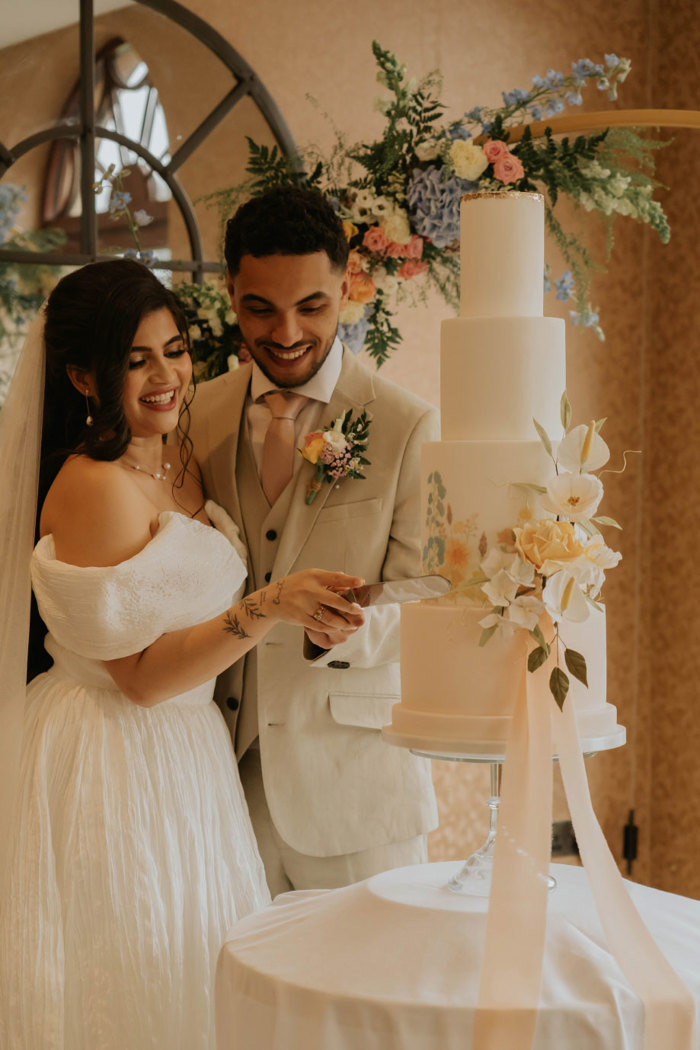 A bride and groom smile as they cut into their four tier wedding cake