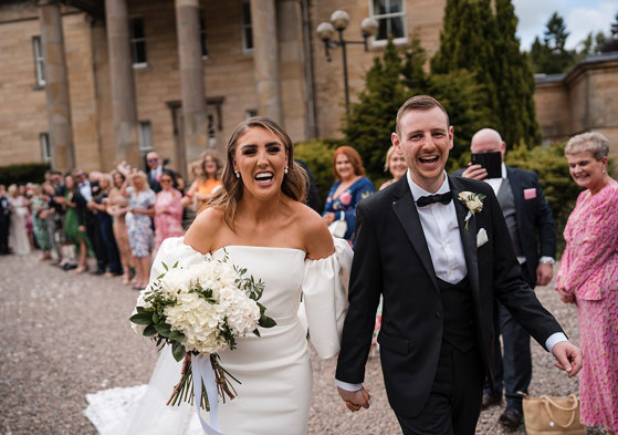 Bride and groom laugh as they leave their ceremony with guests clapping in background