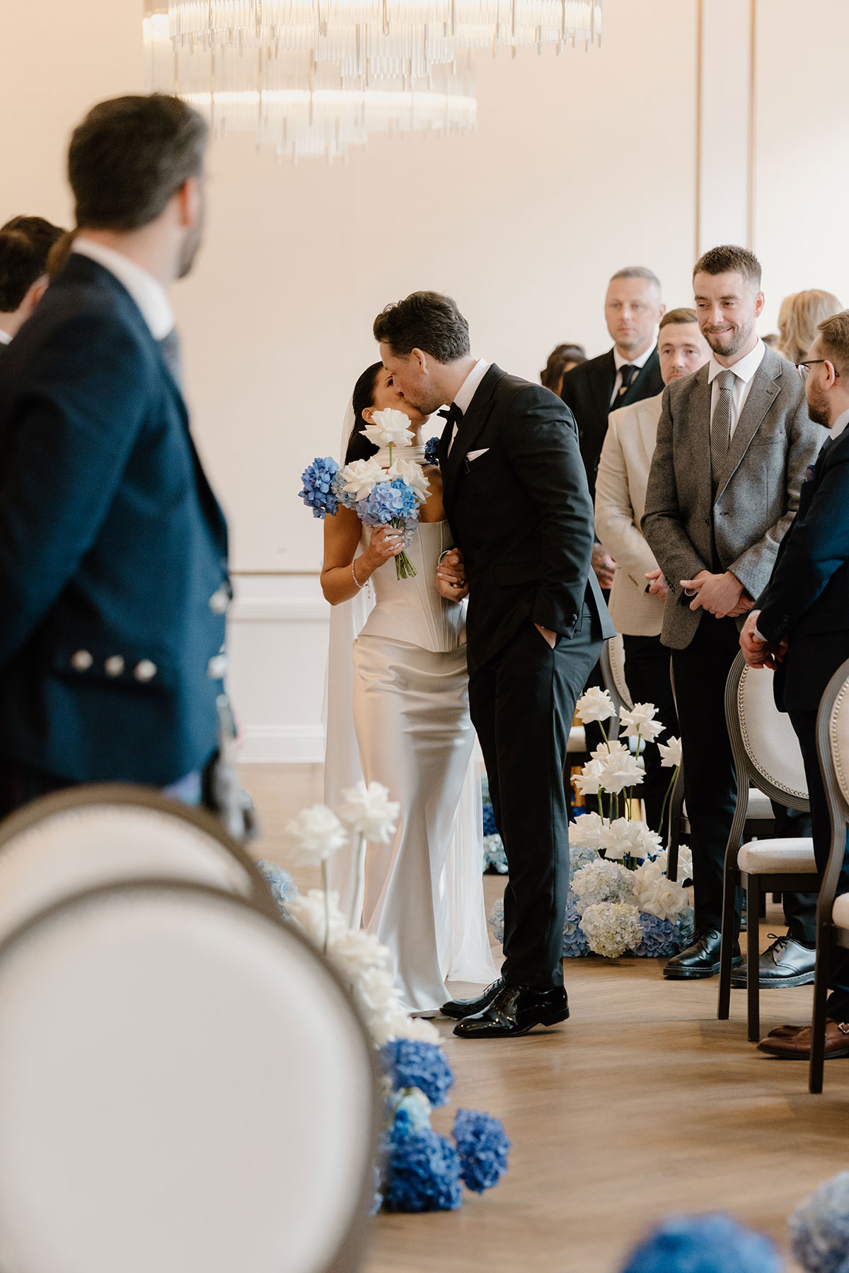 Bride and groom kissing during their wedding ceremony at The Exchange in Glasgow, surrounded by blue and white flowers.