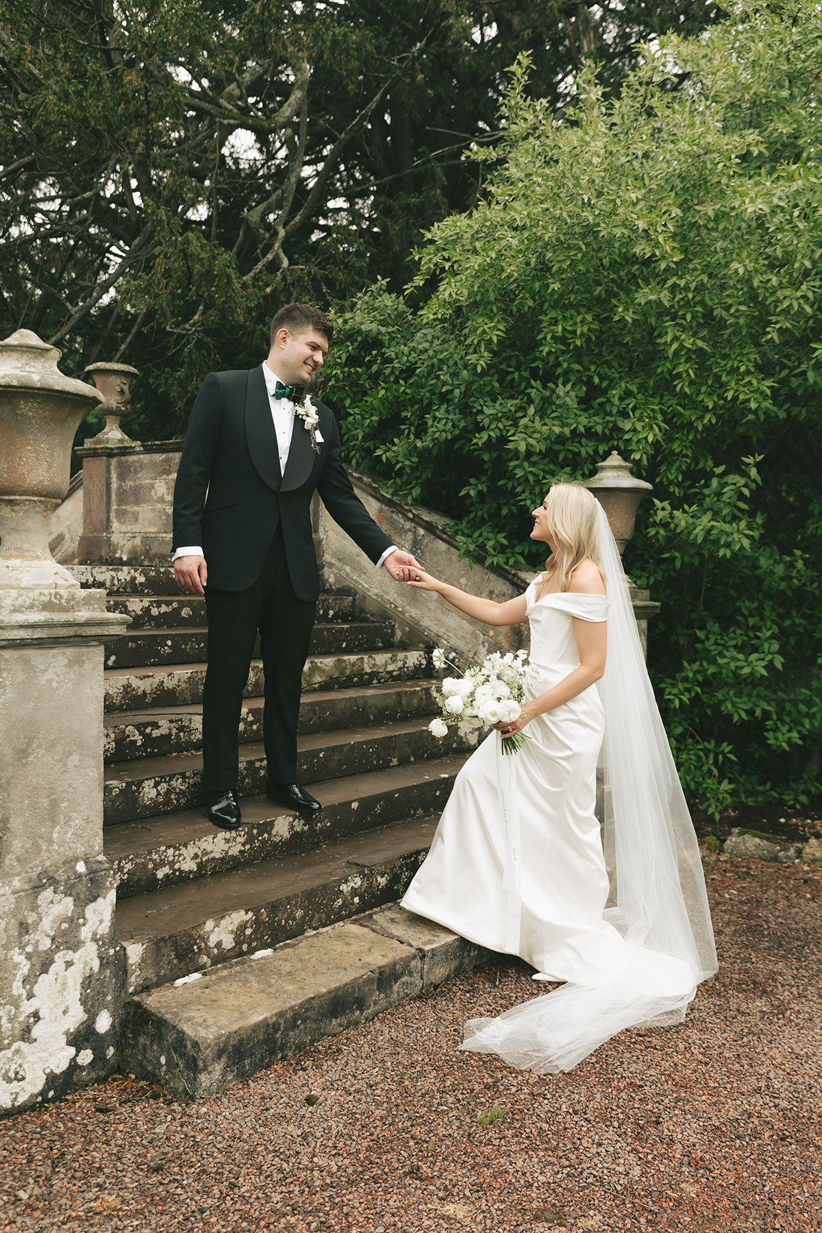 Bride and groom holding hands on stone steps in garden at Gilmerton House East Lothian