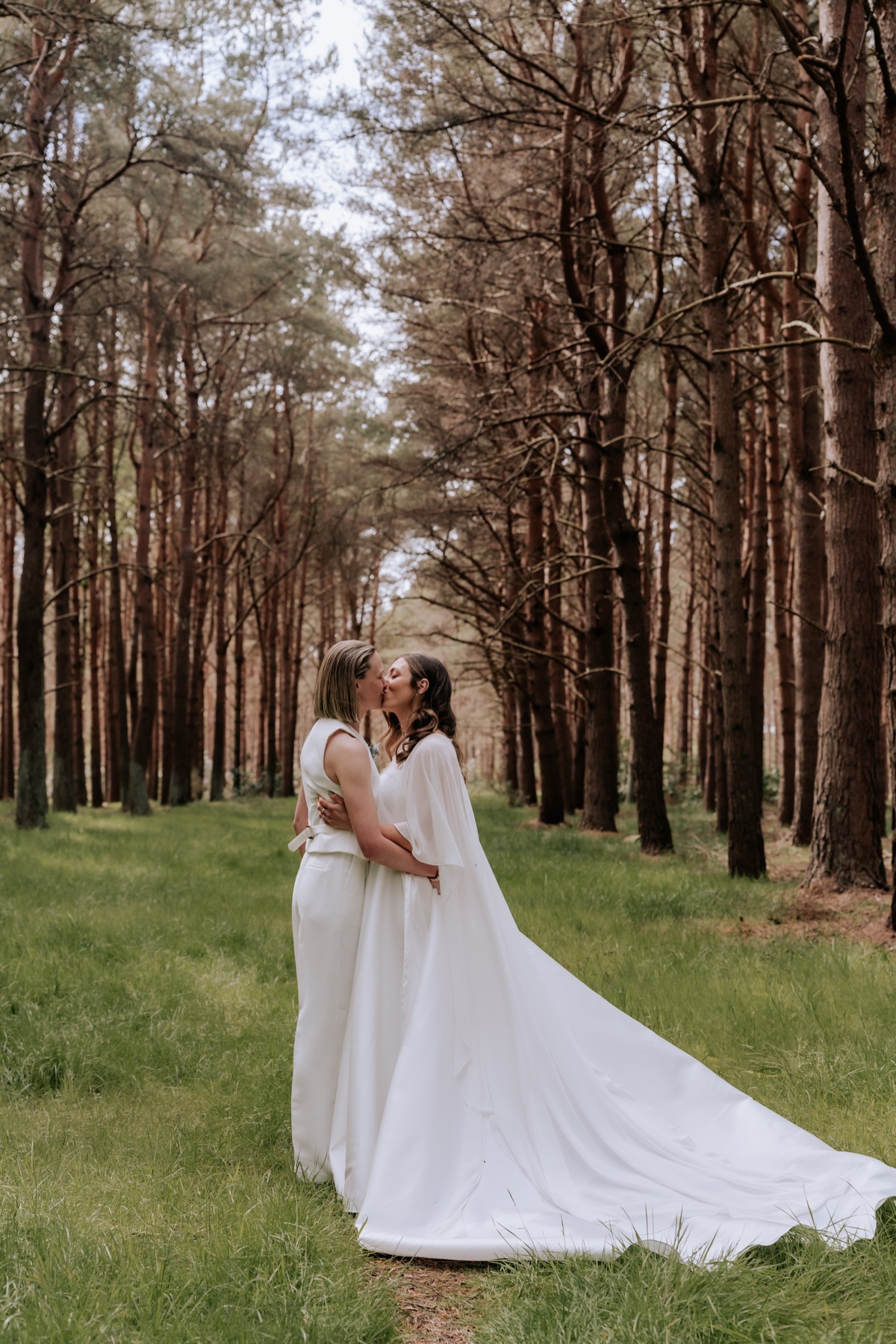 Hannah and Donna kissing among the trees during their Harvest Moon wedding portraits.